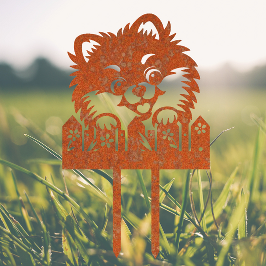 Vrolijke honden tuinprikker Luna achter het Hek, gemaakt van cortenstaal, ideaal voor bloemperken en tuinaccessoires.